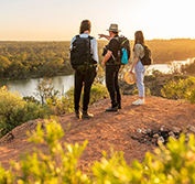 Three people walking on a path above the Murray River in South Australia at sunset, looking out across the water and forest beyond.